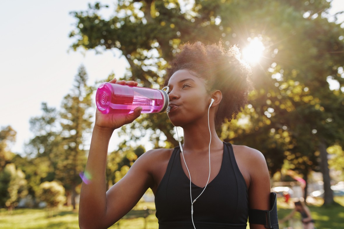 En ung kvinne løper ute og drikker fra vannflasken
